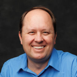 Picture of Darren Hansen, a smiling, balding man in a collared blue shirt.